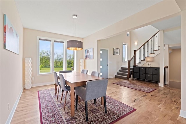 dining space featuring baseboards, light wood-type flooring, and stairs