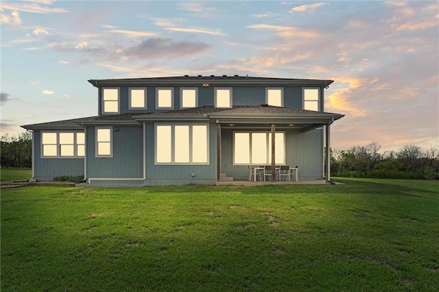 back of property with roof with shingles, a patio, and a yard