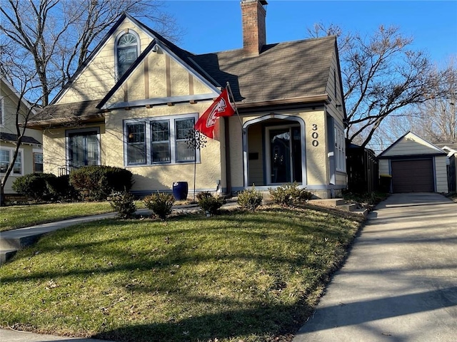 tudor home featuring a garage, an outbuilding, and a front lawn