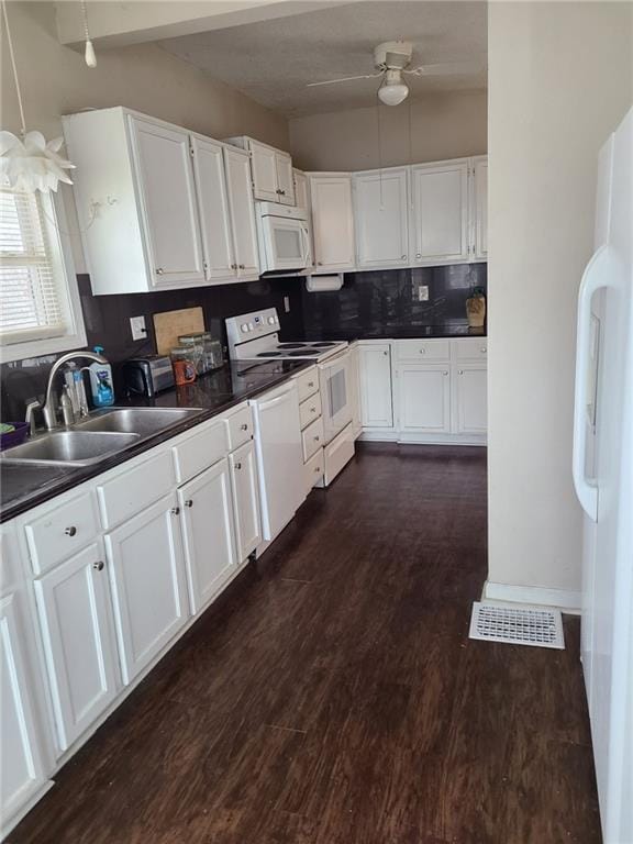 kitchen with white appliances, white cabinets, dark countertops, dark wood-style flooring, and a sink