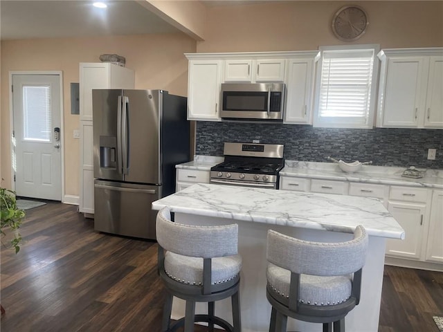 kitchen with appliances with stainless steel finishes, a kitchen bar, white cabinets, and light stone counters