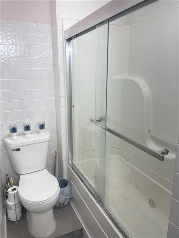 bathroom with enclosed tub / shower combo, tile patterned floors, toilet, and tile walls