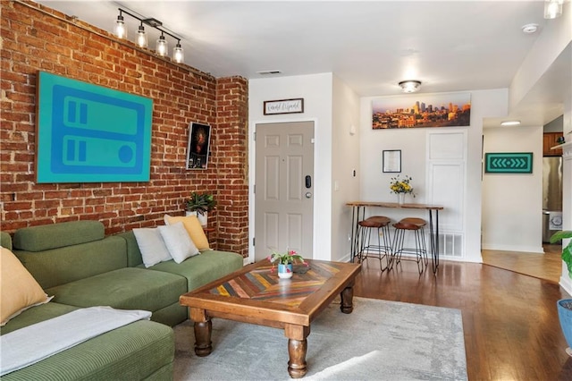 living room with brick wall, track lighting, and dark hardwood / wood-style flooring