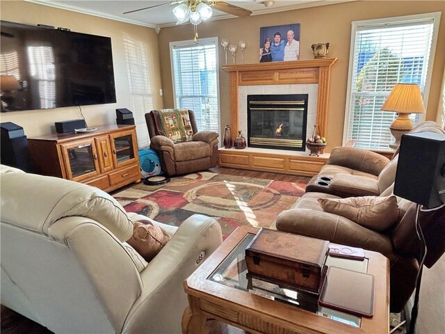 living area with ornamental molding, a tiled fireplace, and a ceiling fan