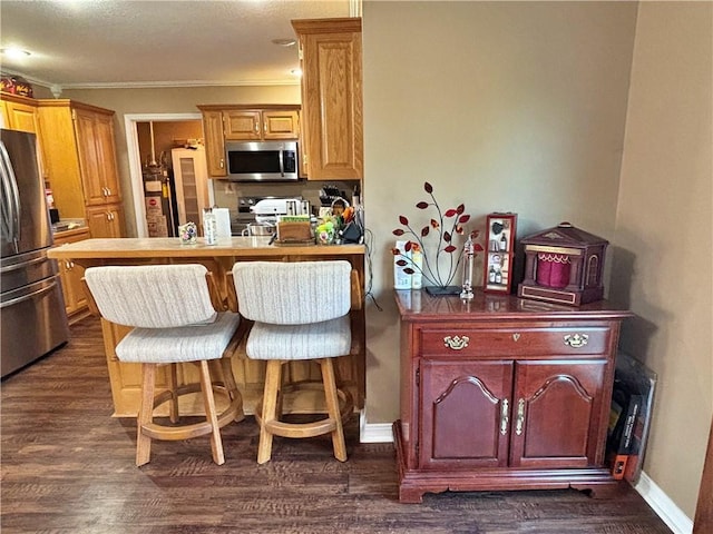 kitchen featuring baseboards, appliances with stainless steel finishes, dark wood-type flooring, crown molding, and a kitchen bar