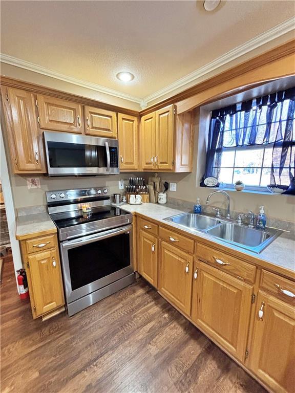 kitchen featuring dark wood finished floors, crown molding, light countertops, appliances with stainless steel finishes, and a sink