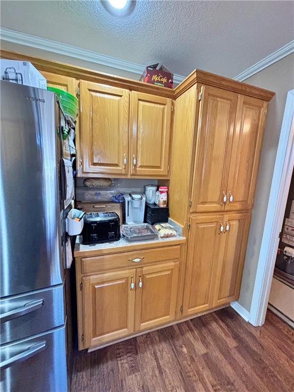 kitchen with a textured ceiling, dark wood-type flooring, light countertops, ornamental molding, and freestanding refrigerator