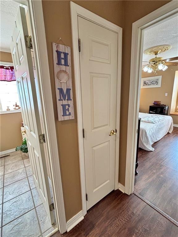 hall featuring a textured ceiling, baseboards, and wood finished floors