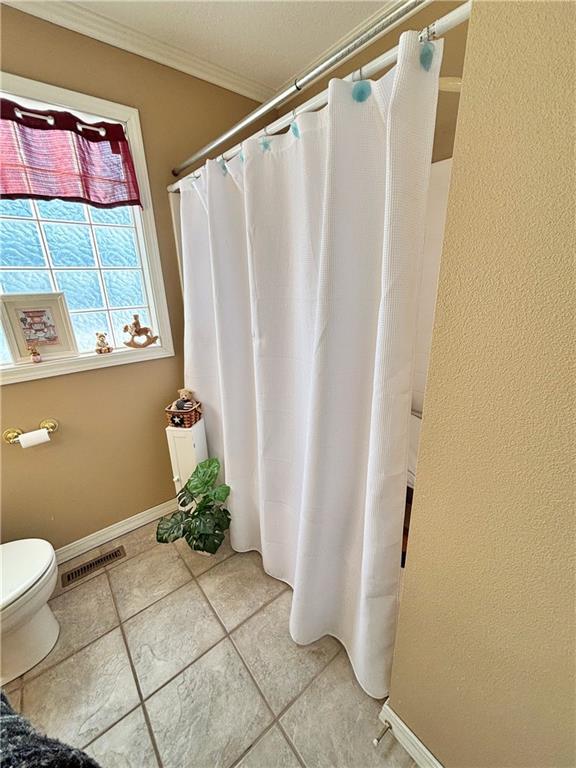 bathroom with toilet, ornamental molding, visible vents, and baseboards