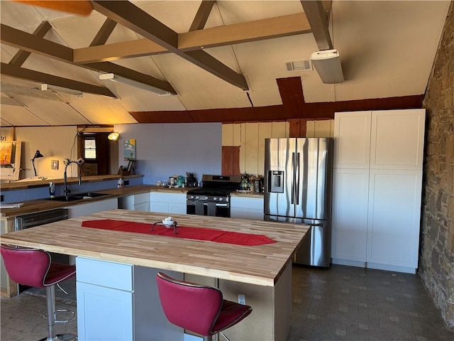 kitchen with white cabinetry, stainless steel appliances, wooden counters, and a kitchen bar