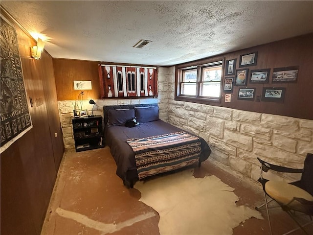 bedroom featuring concrete floors, a textured ceiling, and wood walls