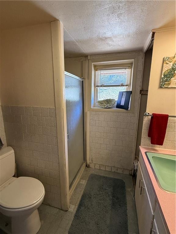 bathroom with tile walls, vanity, an enclosed shower, toilet, and a textured ceiling