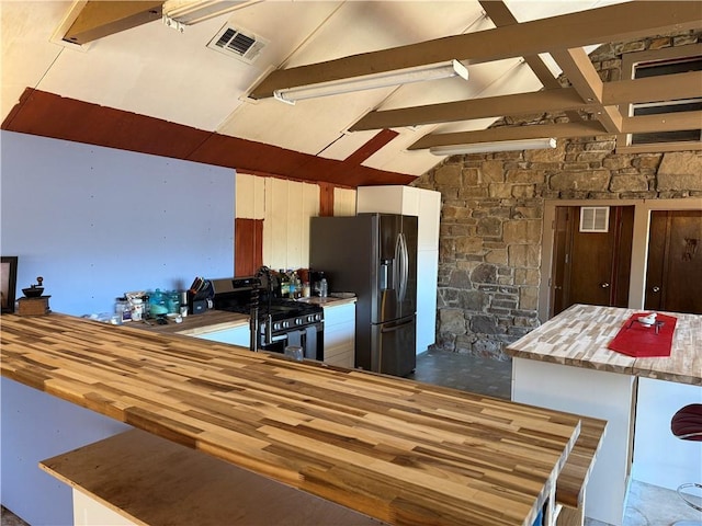 kitchen featuring stainless steel appliances, white cabinets, wooden counters, and lofted ceiling with beams