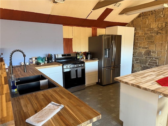 kitchen with sink, appliances with stainless steel finishes, vaulted ceiling with beams, white cabinets, and wood counters