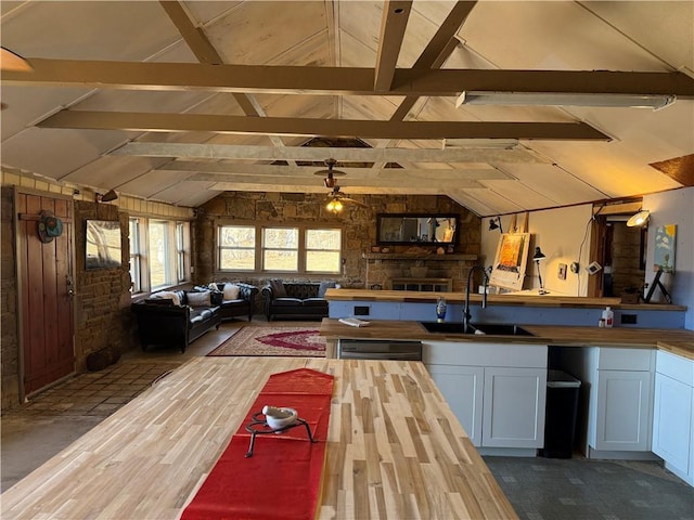 kitchen featuring wood walls, lofted ceiling with beams, white cabinetry, sink, and butcher block counters