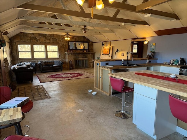 kitchen with a stone fireplace, sink, vaulted ceiling with beams, wooden counters, and concrete floors