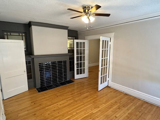 interior space with ceiling fan, light hardwood / wood-style floors, a textured ceiling, a tiled fireplace, and french doors