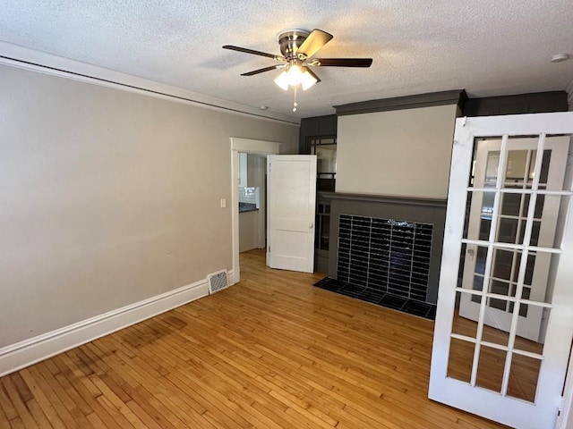 empty room featuring ceiling fan, a tiled fireplace, a textured ceiling, and light wood-type flooring