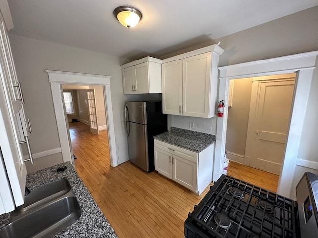 kitchen with stainless steel refrigerator, black gas stove, white cabinets, dark stone counters, and light wood-type flooring