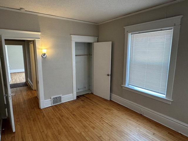 unfurnished bedroom featuring ornamental molding, a closet, a textured ceiling, and light wood-type flooring