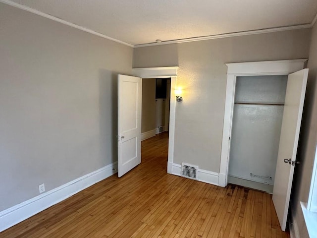 unfurnished bedroom featuring ornamental molding, light hardwood / wood-style floors, and a closet