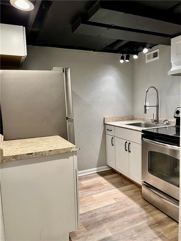 kitchen with stainless steel appliances, sink, light hardwood / wood-style flooring, and white cabinets