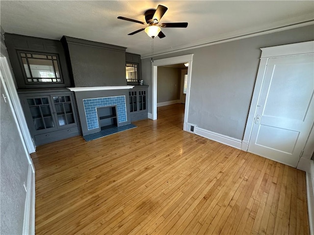 unfurnished living room with ceiling fan, crown molding, a fireplace, and light hardwood / wood-style flooring