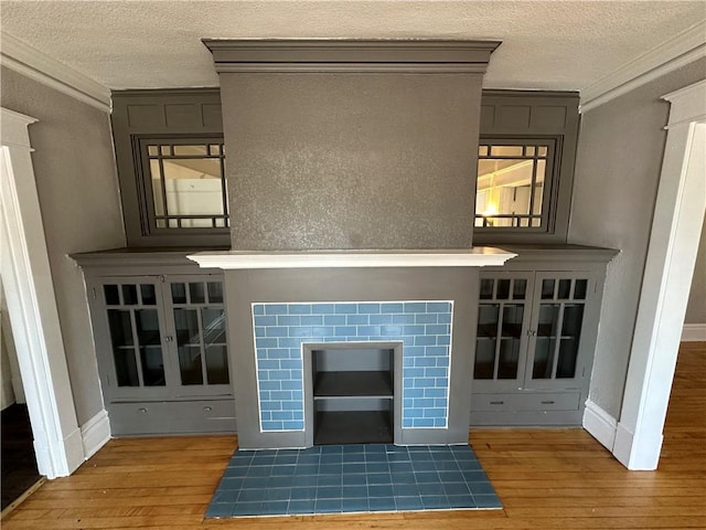 unfurnished living room with ornamental molding, wood-type flooring, a tile fireplace, and a textured ceiling