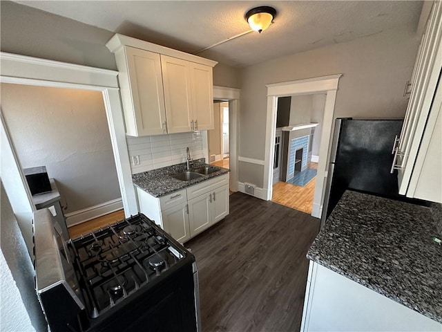 kitchen featuring sink, stainless steel refrigerator, white cabinetry, black range with gas stovetop, and dark stone counters