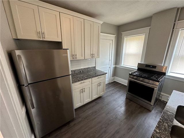 kitchen featuring white cabinetry, tasteful backsplash, appliances with stainless steel finishes, dark hardwood / wood-style floors, and dark stone counters