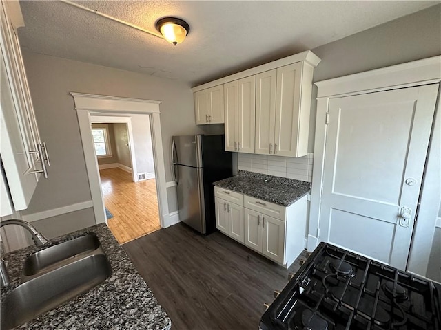 kitchen with stainless steel refrigerator, sink, dark stone countertops, white cabinets, and dark hardwood / wood-style flooring