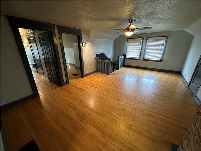 additional living space featuring ceiling fan, vaulted ceiling, a textured ceiling, and light wood-type flooring