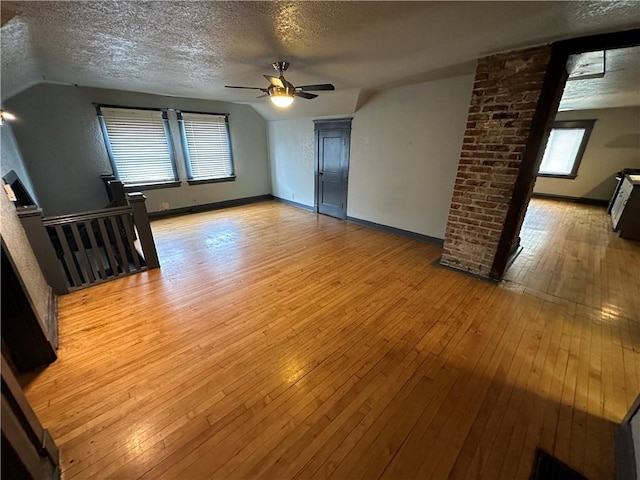 empty room with vaulted ceiling, a textured ceiling, and light hardwood / wood-style flooring