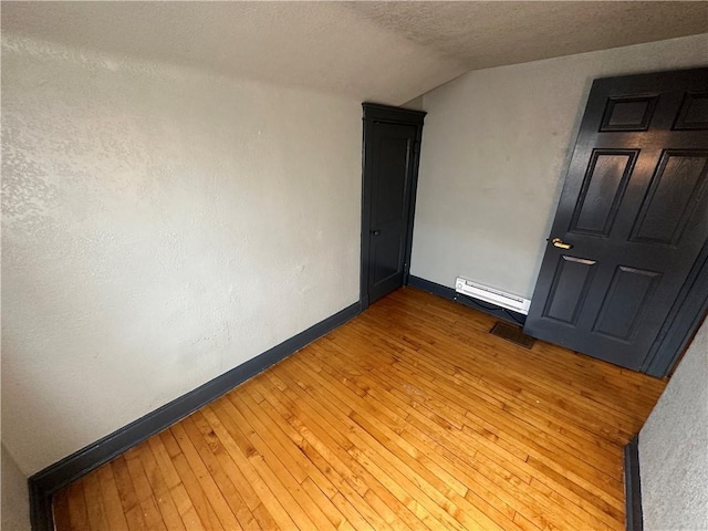 unfurnished room featuring a baseboard radiator, vaulted ceiling, a textured ceiling, and light wood-type flooring