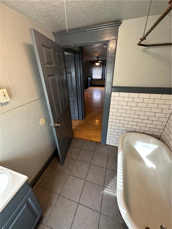 interior space featuring a tub, vanity, ceiling fan, tile patterned floors, and a textured ceiling