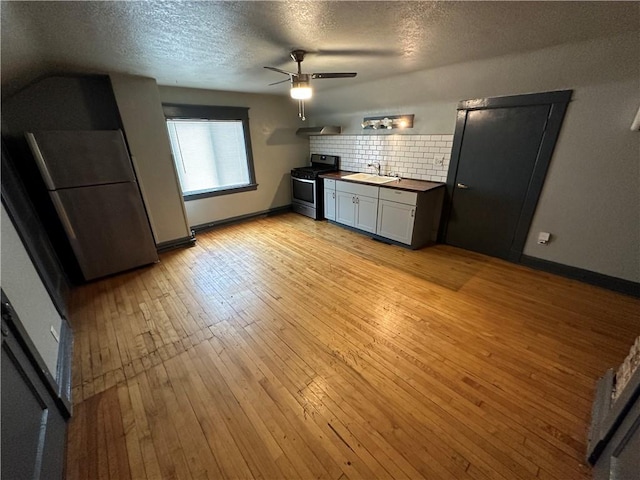 kitchen with appliances with stainless steel finishes, wood counters, tasteful backsplash, sink, and light wood-type flooring