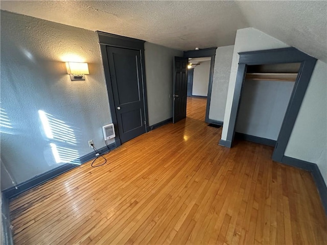 unfurnished bedroom with hardwood / wood-style floors, vaulted ceiling, a closet, and a textured ceiling