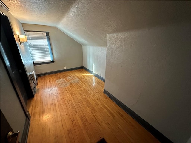 bonus room with vaulted ceiling, a textured ceiling, and light hardwood / wood-style floors