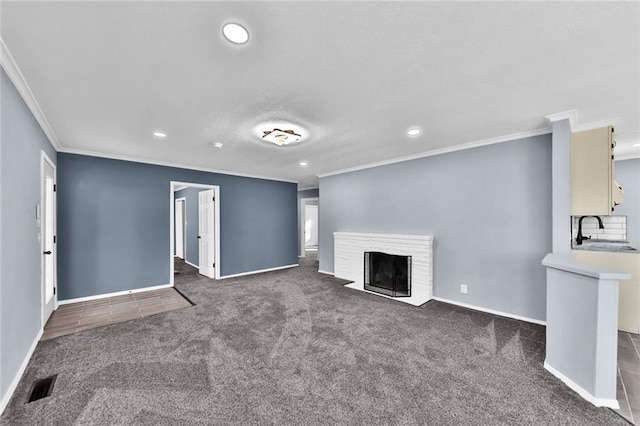 unfurnished living room featuring carpet, visible vents, a fireplace with flush hearth, a sink, and baseboards