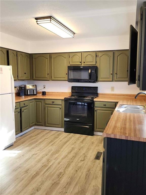 kitchen featuring sink, butcher block countertops, green cabinetry, light wood-type flooring, and black appliances