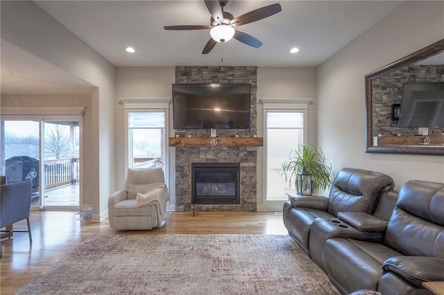 living room featuring ceiling fan, a stone fireplace, and light wood-type flooring