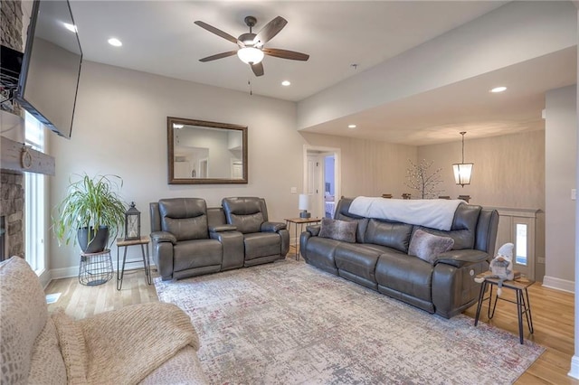 living room with ceiling fan, a stone fireplace, and light hardwood / wood-style flooring