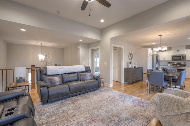 living room featuring ceiling fan with notable chandelier and light hardwood / wood-style flooring