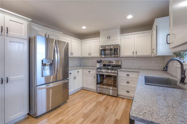 kitchen featuring sink, light wood-type flooring, appliances with stainless steel finishes, light stone countertops, and white cabinets