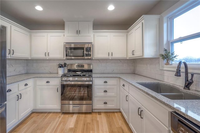 kitchen featuring appliances with stainless steel finishes, white cabinetry, sink, light stone counters, and light wood-type flooring