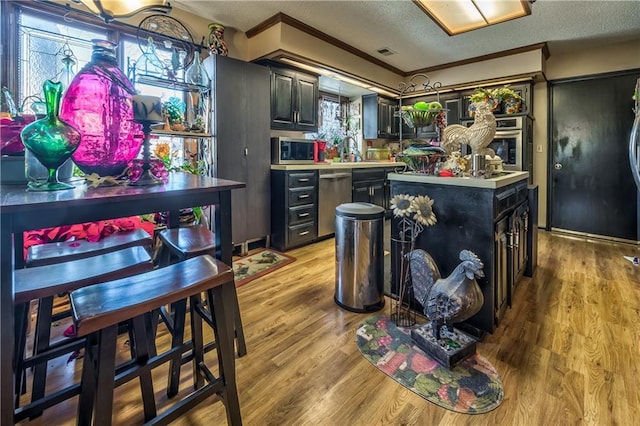 kitchen featuring appliances with stainless steel finishes, a center island, light hardwood / wood-style floors, crown molding, and a textured ceiling