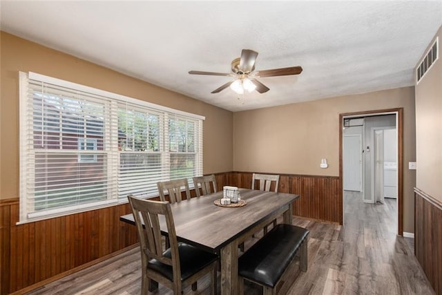 dining area featuring hardwood / wood-style flooring, ceiling fan, and wood walls