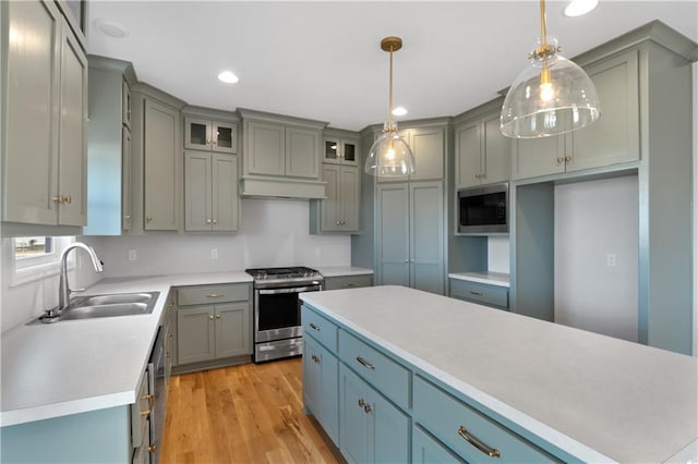 kitchen with gray cabinets, appliances with stainless steel finishes, pendant lighting, sink, and light hardwood / wood-style floors