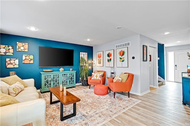 living room featuring light wood-style flooring, stairway, visible vents, and baseboards