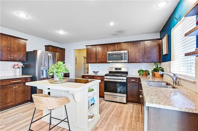 kitchen with light wood finished floors, stainless steel appliances, a sink, and a kitchen breakfast bar